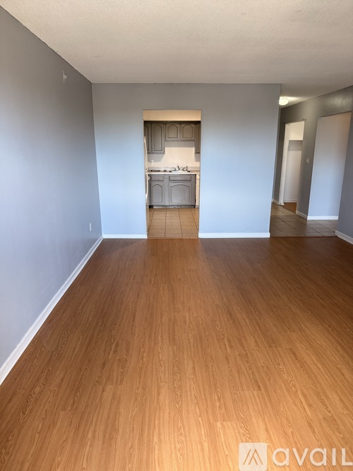 A room with wooden flooring and a kitchen in the background.
