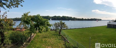 A view of a lake from a grassy area with a fence and trees.