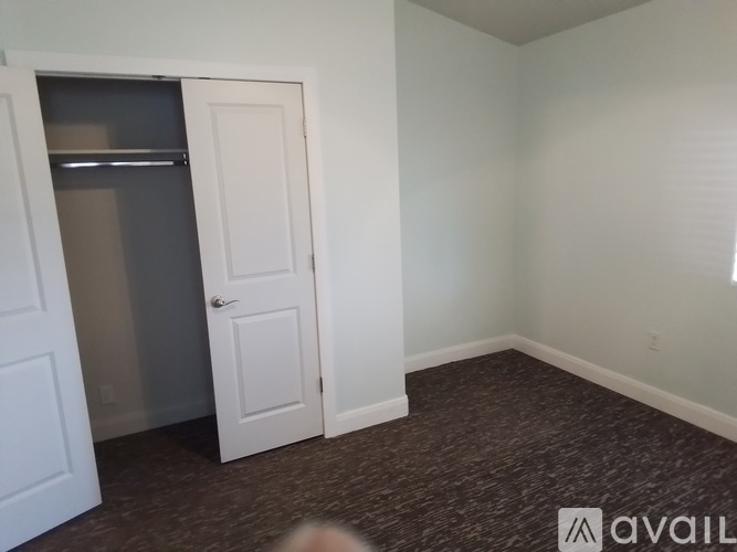 A room with a carpeted floor, a white door, and a window with blinds.