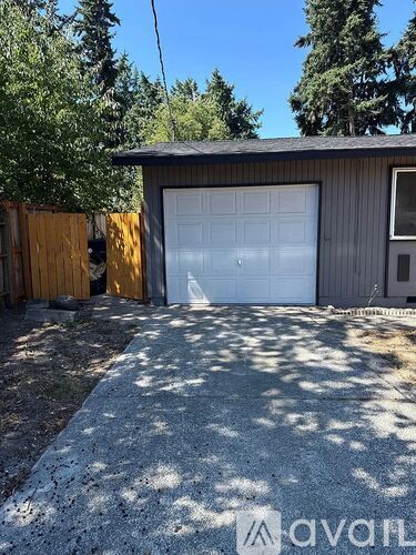 A garage with a white door is surrounded by trees and a wooden fence.