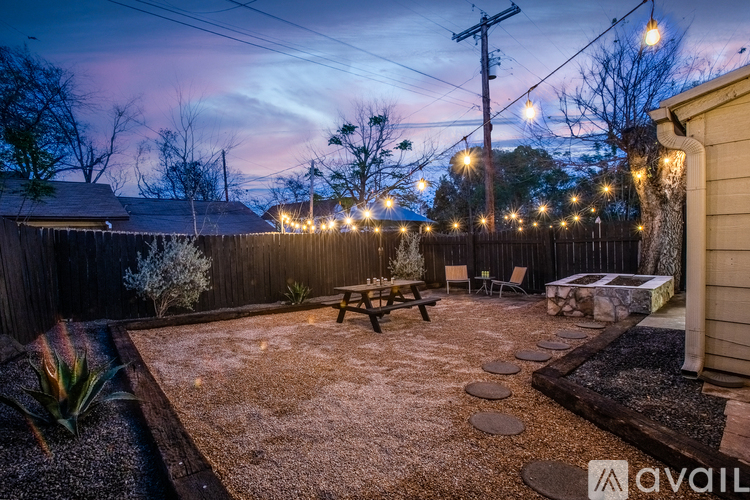 A backyard with a picnic table and lights strung up on a fence.