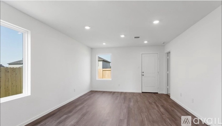 A room with wooden floors and white walls, with a window on the left side.