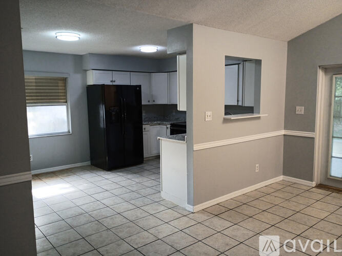 A kitchen area with a black refrigerator, white countertops, and a window with blinds.