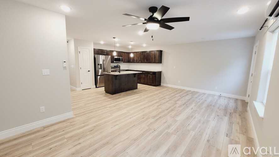 A spacious room with a kitchen area in the background and a wooden floor.