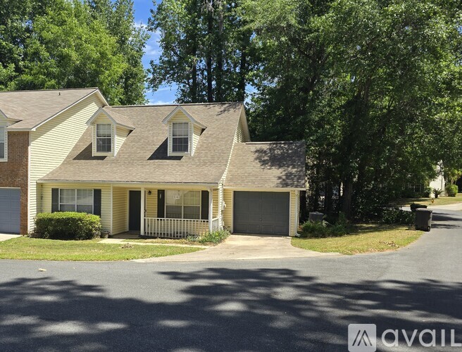 A house with a garage is surrounded by trees and has a driveway in front.