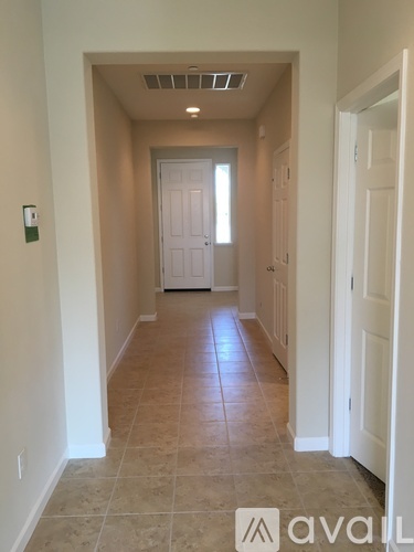 A hallway with tiled floors and white walls leading to a white door.
