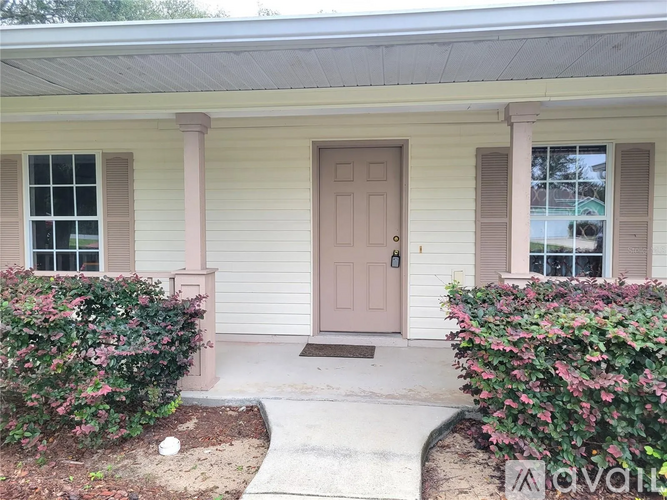 A house with a brown door and windows with bushes in front.