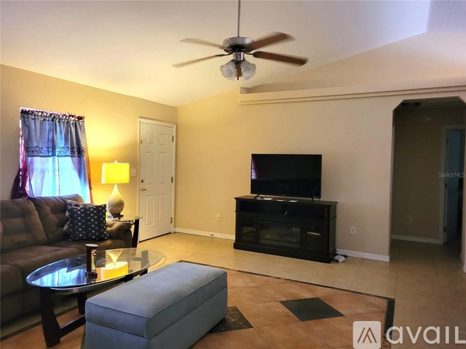 A living room with a brown couch, a glass table, a television, and a ceiling fan.