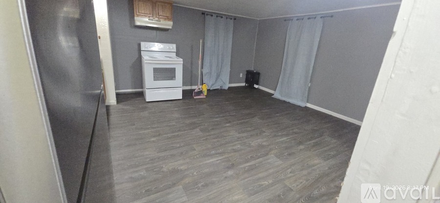 A kitchen with a refrigerator, oven, and a broom.