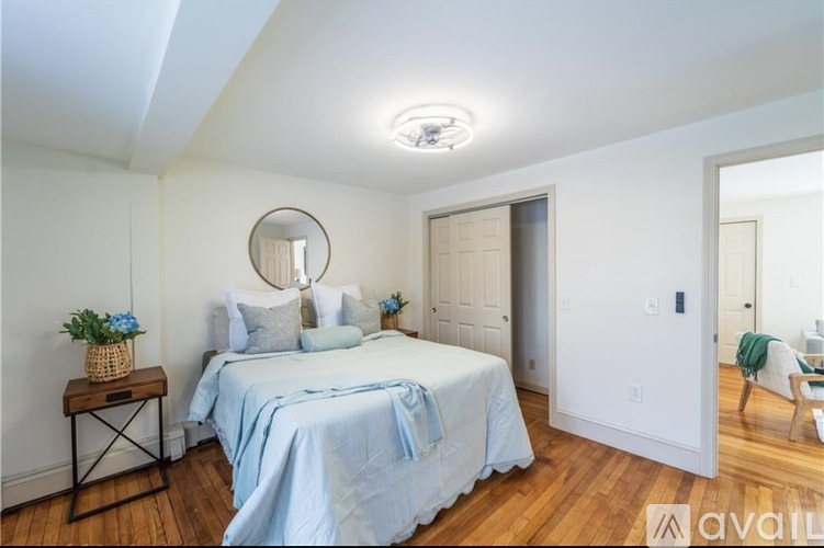 A bedroom with a round mirror, a bed with a blue blanket, and a wooden table with a plant on it.