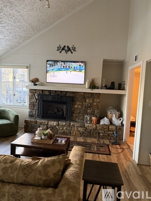 A living room with a stone fireplace and a television mounted above it.