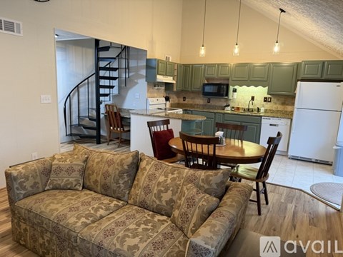 A living room with a couch, chairs, and a kitchen area in the background.