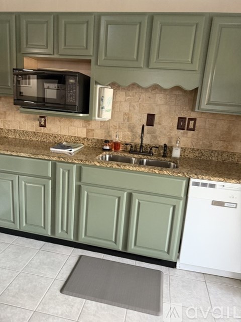 A kitchen with green cabinets and a black microwave.