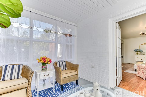 A living room with a white sofa, a wicker chair, and a small table with a vase of flowers on it.