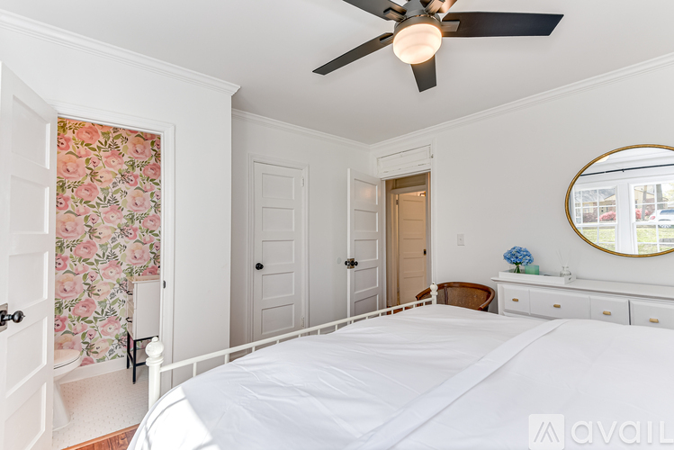 A bedroom with a large bed, a ceiling fan, and a round mirror on the wall.