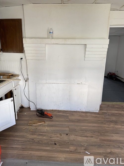 A room with a white wall and wooden floor with a tool on it.