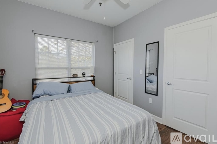 A bedroom with a bed, a guitar, and a window with blinds.