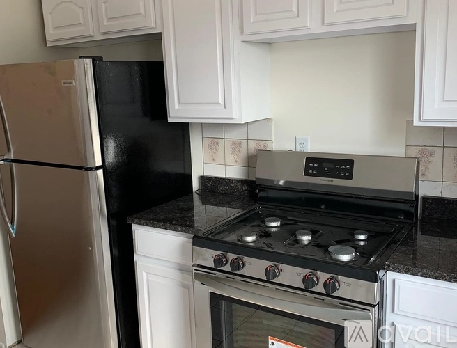 A black refrigerator stands next to a stove in a kitchen.