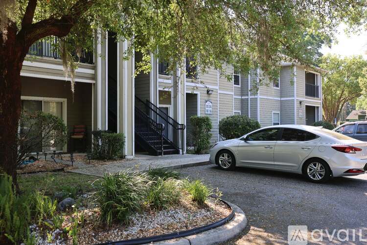 A silver car is parked in front of a building with a tree in front of it.
