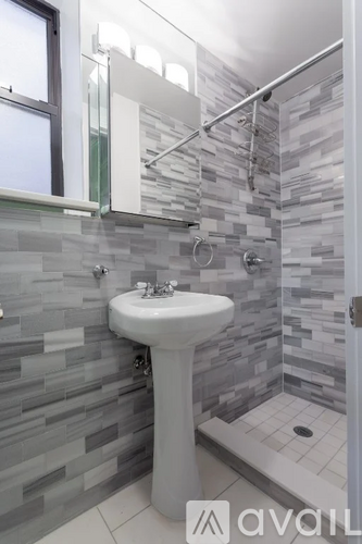 A bathroom with a white pedestal sink and grey tiled walls.