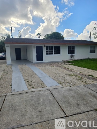 A white house with a blue door and windows is surrounded by a concrete driveway.