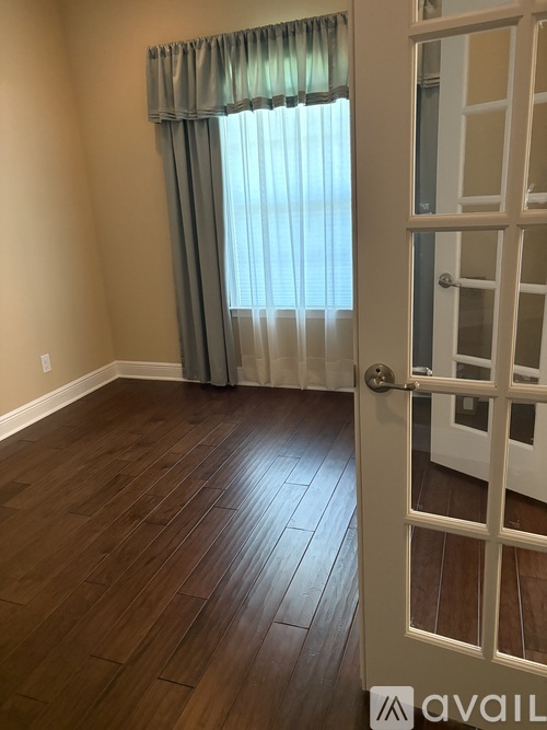 A room with a wooden floor and a door leading to another room.