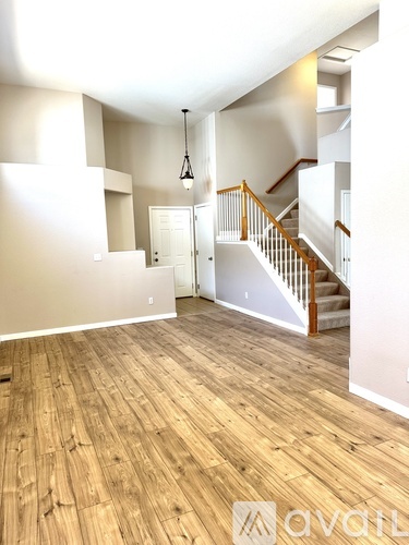 A spacious room with wooden flooring and a staircase.