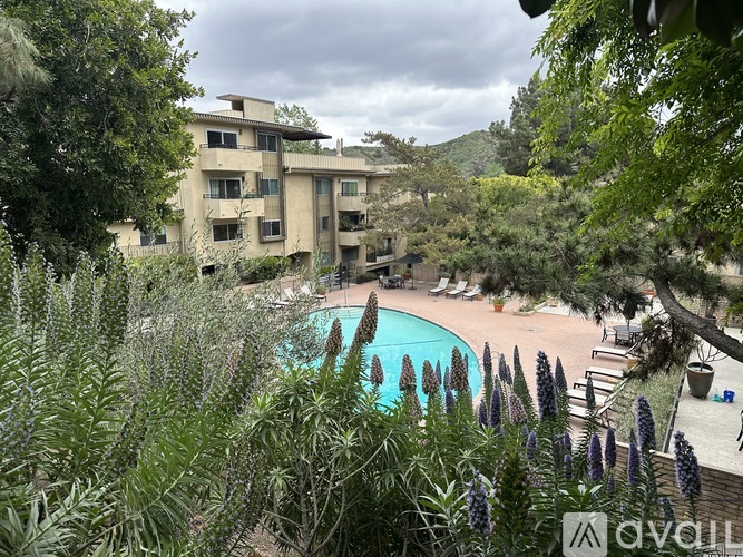 A pool surrounded by greenery and a building in the background.
