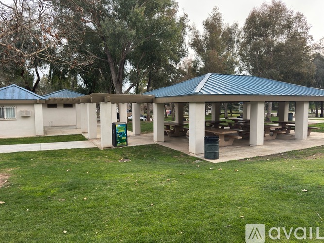 A pavilion with a blue roof is surrounded by a grassy area and trees.