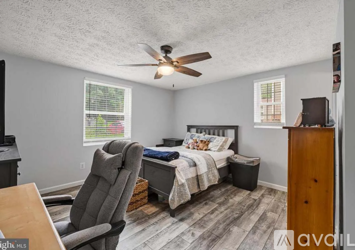 A bedroom with a bed, chair, and a ceiling fan.