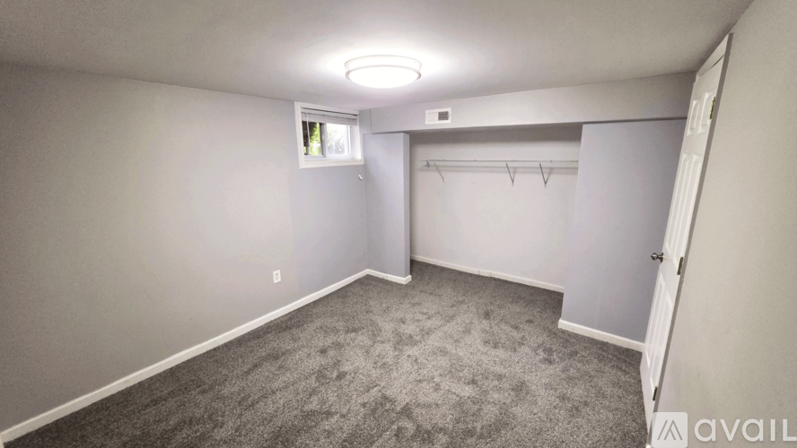 A sparsely furnished bedroom with a grey carpet and a window.