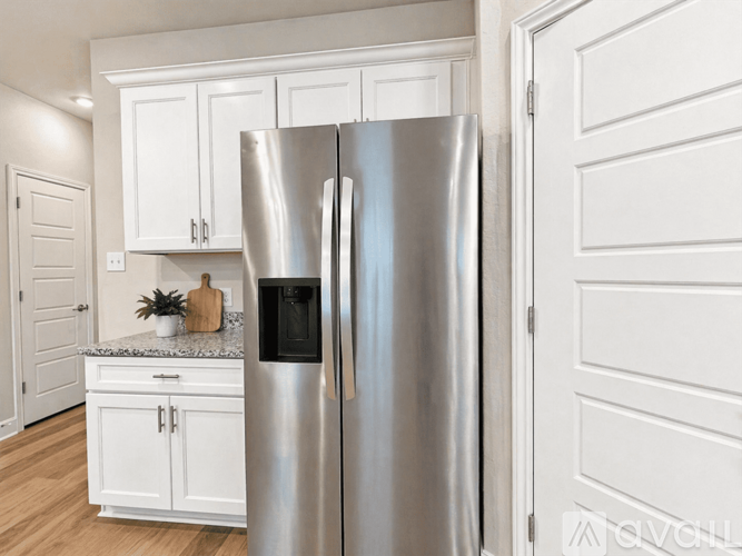 A stainless steel refrigerator stands in a kitchen with white cabinets.