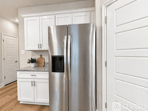 A stainless steel refrigerator stands in a kitchen with white cabinets.