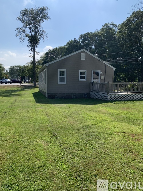 A small house with a grey roof and a white fence is surrounded by a grassy area.