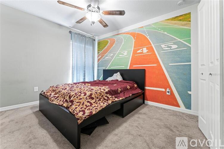 A bedroom with a bed, a ceiling fan, and a racing track mural on the wall.