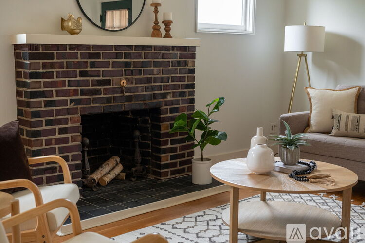A living room with a brick fireplace, a wooden chair, a round table with a plant on it, and a lamp.