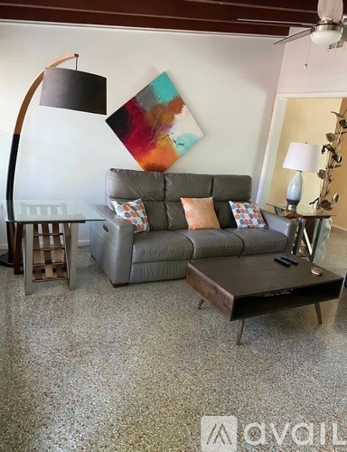 A living room with a grey couch, a wooden floor lamp, and a painting on the wall.