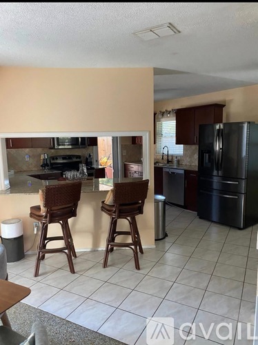 A kitchen with a black refrigerator and brown bar stools.