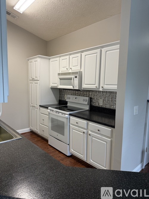 A kitchen with white cabinets and black countertops.