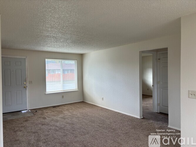A room with a carpeted floor, two doors, and a window with a view of a building outside.