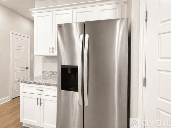 A stainless steel refrigerator stands in a kitchen with white cabinets.