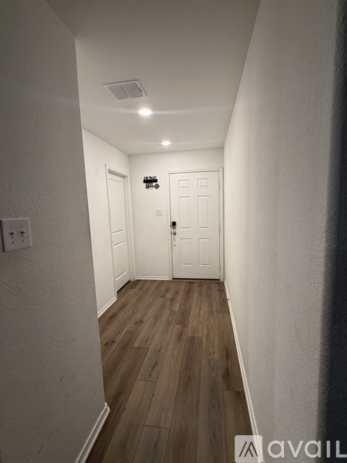 A narrow hallway with a white door and wooden floor.