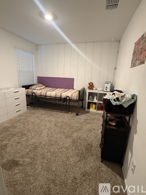 A bedroom with a bed, dresser, and a window with blinds.