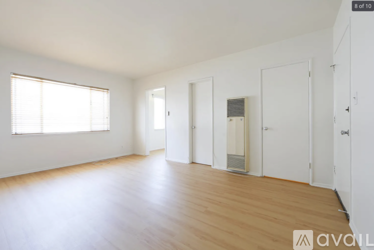 A spacious room with wooden floors and white walls, featuring a window with blinds and a radiator on the wall.