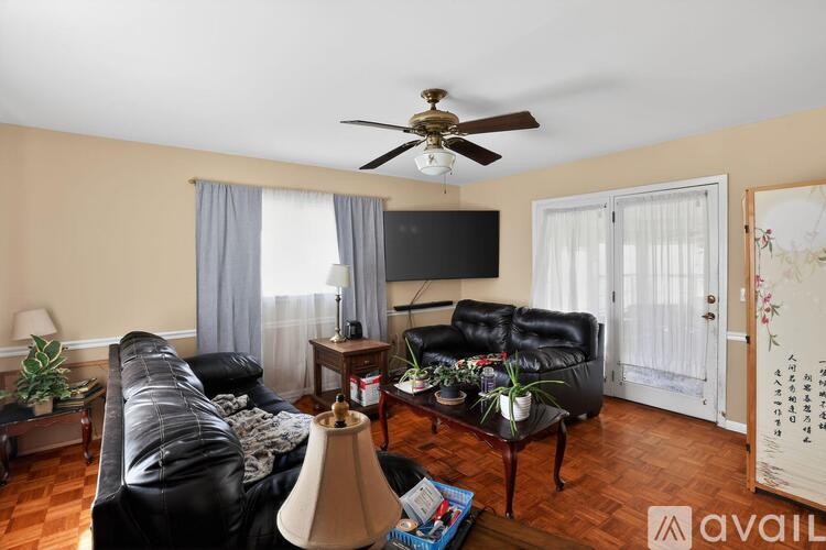 A living room with a black leather couch and a ceiling fan.