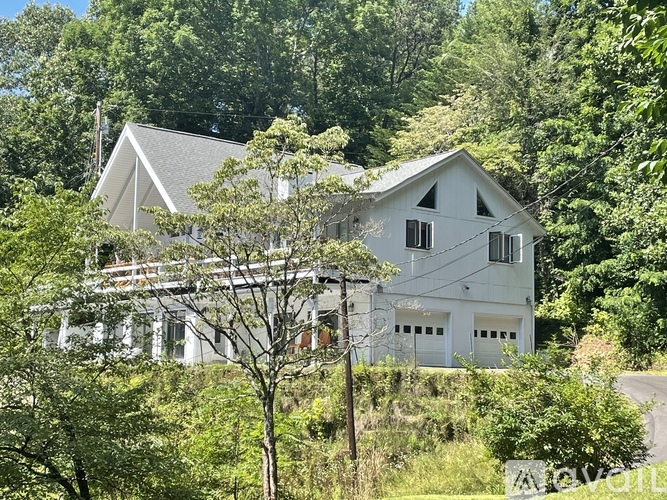 A white house with a grey roof is surrounded by green trees.