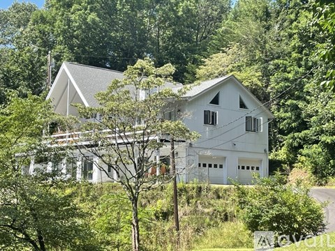 A white house with a grey roof is surrounded by green trees.