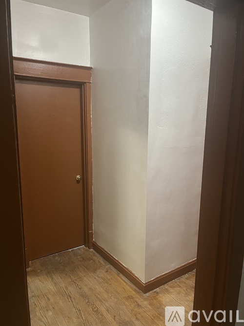 A brown door is in a room with wooden floors and white walls.