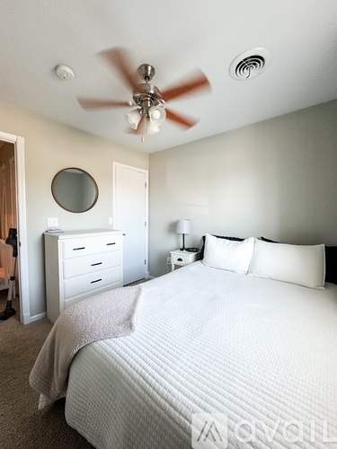 A bedroom with a large bed, a ceiling fan, and a mirror on the wall.