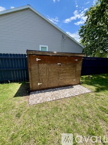 A shed with a wooden door and a window is situated in a grassy area.